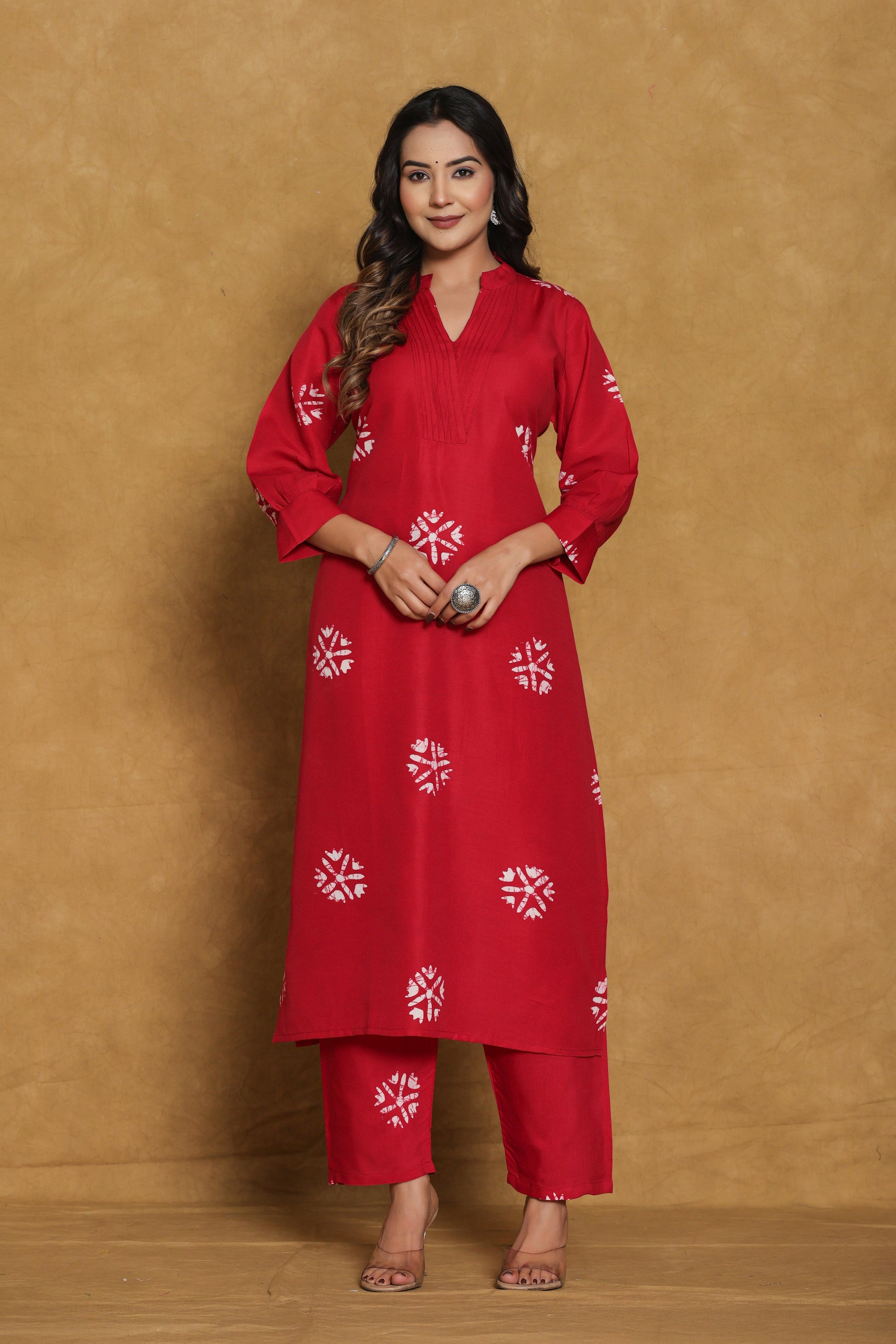Woman wearing a red traditional outfit with white patterns against a brown background