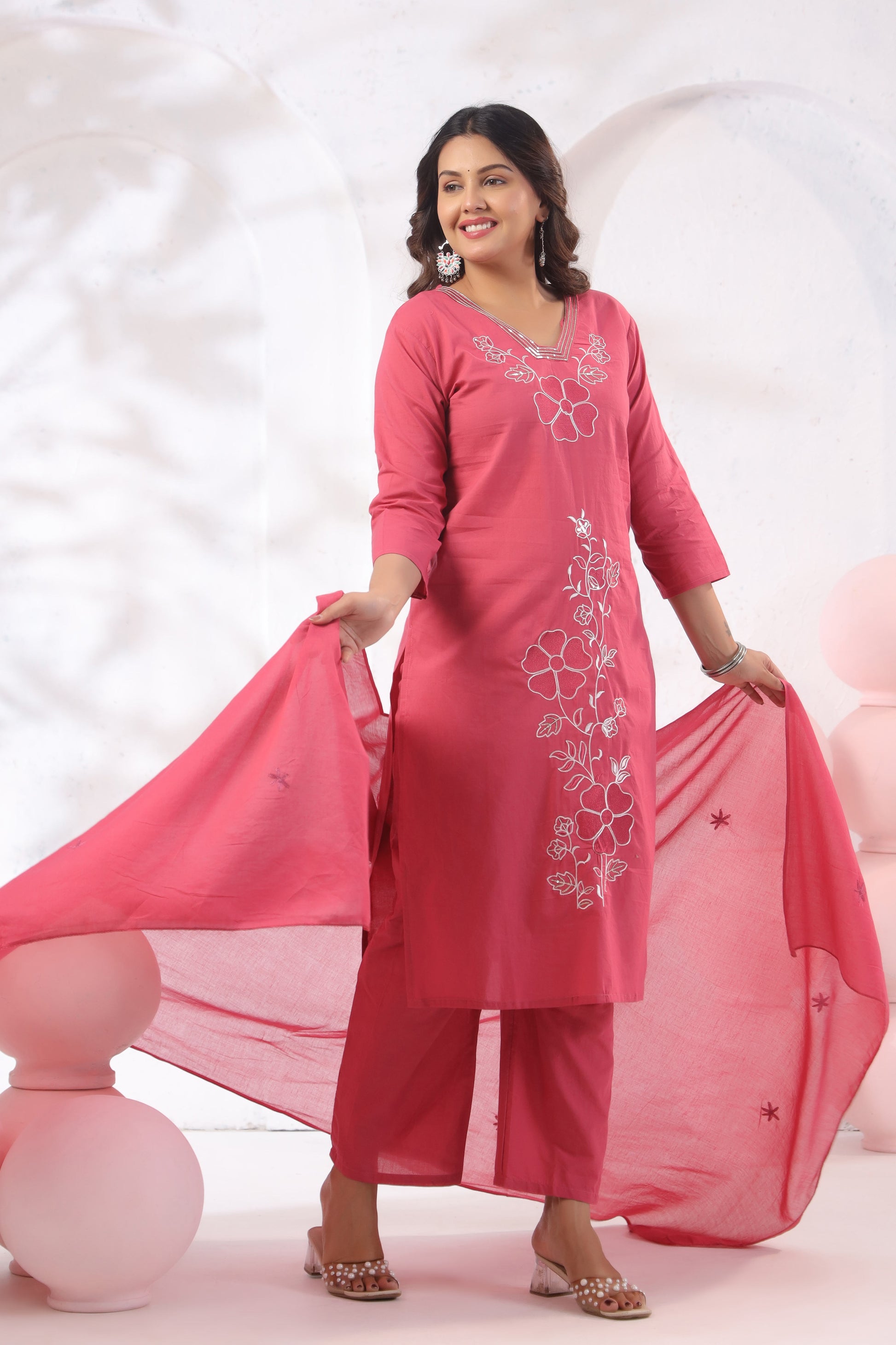 Woman wearing a pink traditional outfit with floral embroidery on a white background
